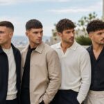 Six handsome male models showcasing different low maintenance haircuts for men including buzz cut, crew cut, French crop, textured crop, curly fade, and bro flow hairstyles.